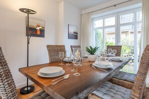 A dining area with a wooden table set for four, surrounded by wicker chairs, with artwork on the walls and a floor lamp.