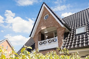 Una casa con fachada de ladrillo, un frente con forma triangular y un balcón con barandillas blancas.