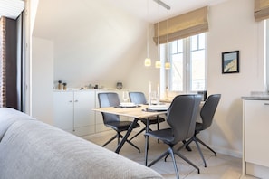 Un comedor moderno y bien iluminado con una mesa de madera, sillas negras y una cocina al fondo.
