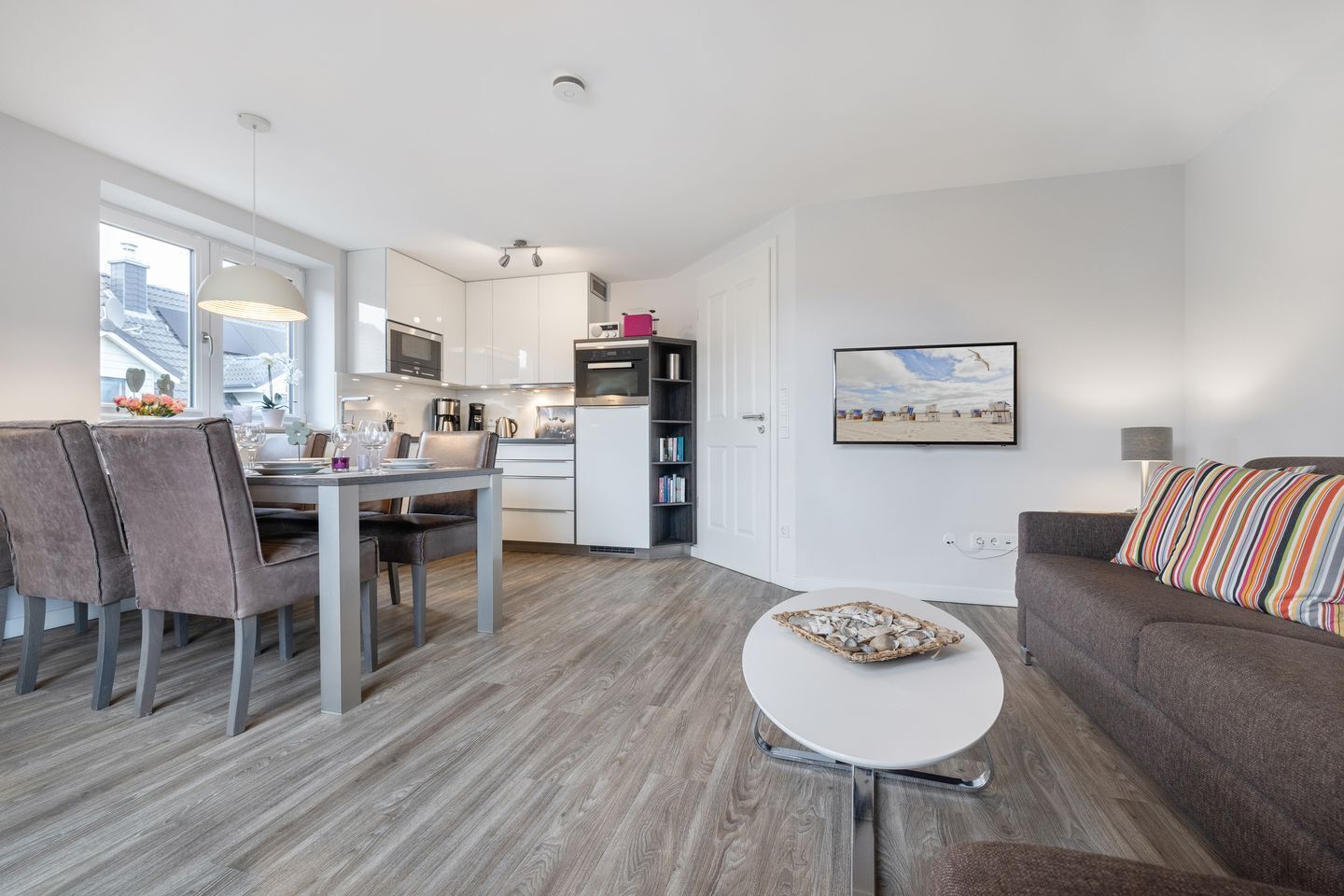 A modern living room with a dining area, a kitchen, and a sofa with striped cushions.
