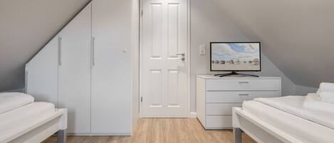 A modern bedroom with a sloped ceiling, white furniture, and a television on a dresser.