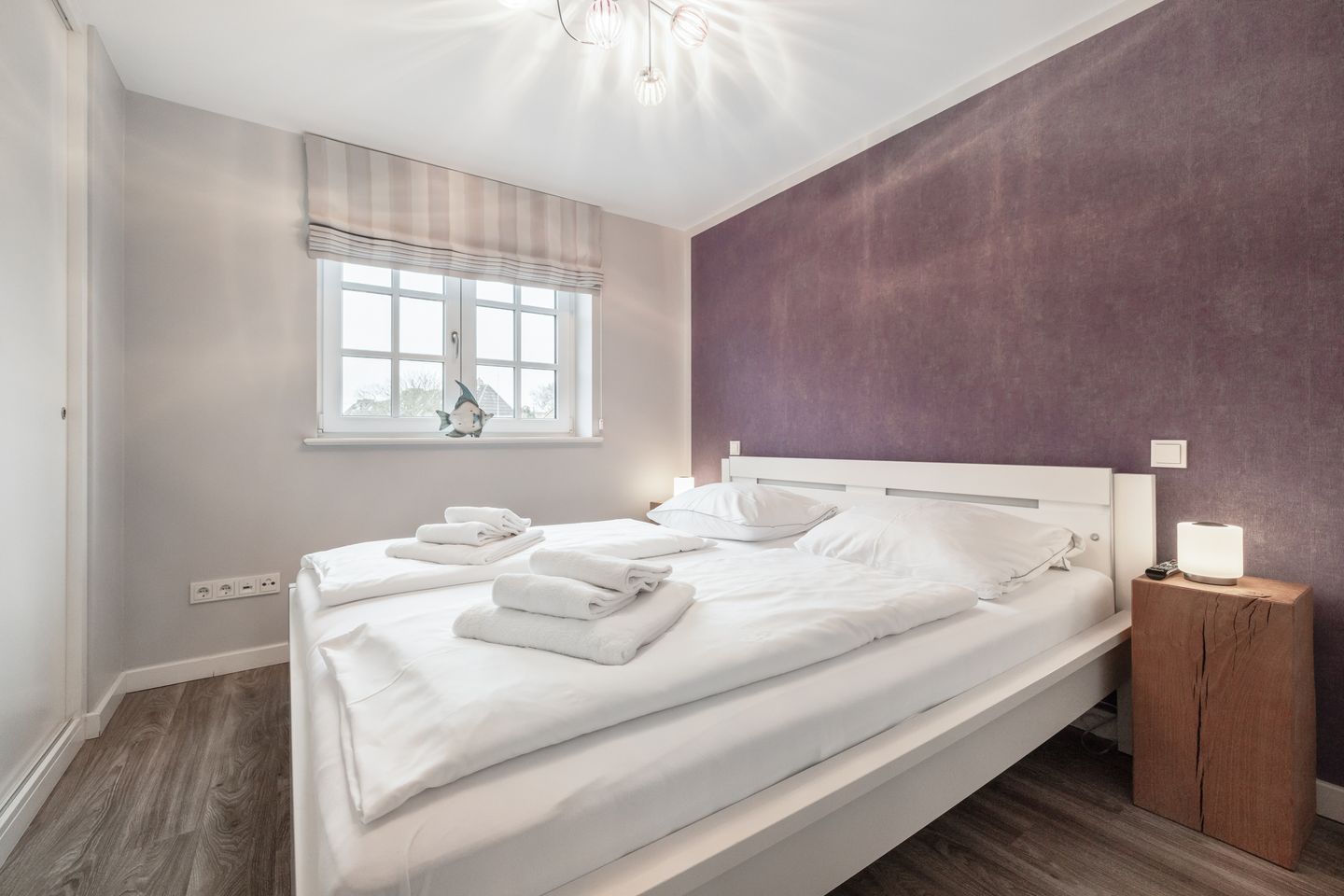 Een moderne slaapkamer met een groot bed, een nachtkastje met lamp, een raam met gordijnen en een wandplank.