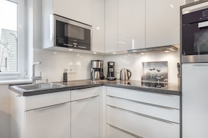 A modern kitchen with white cabinets, stainless steel appliances, a coffee maker, and a wine glass on the counter.