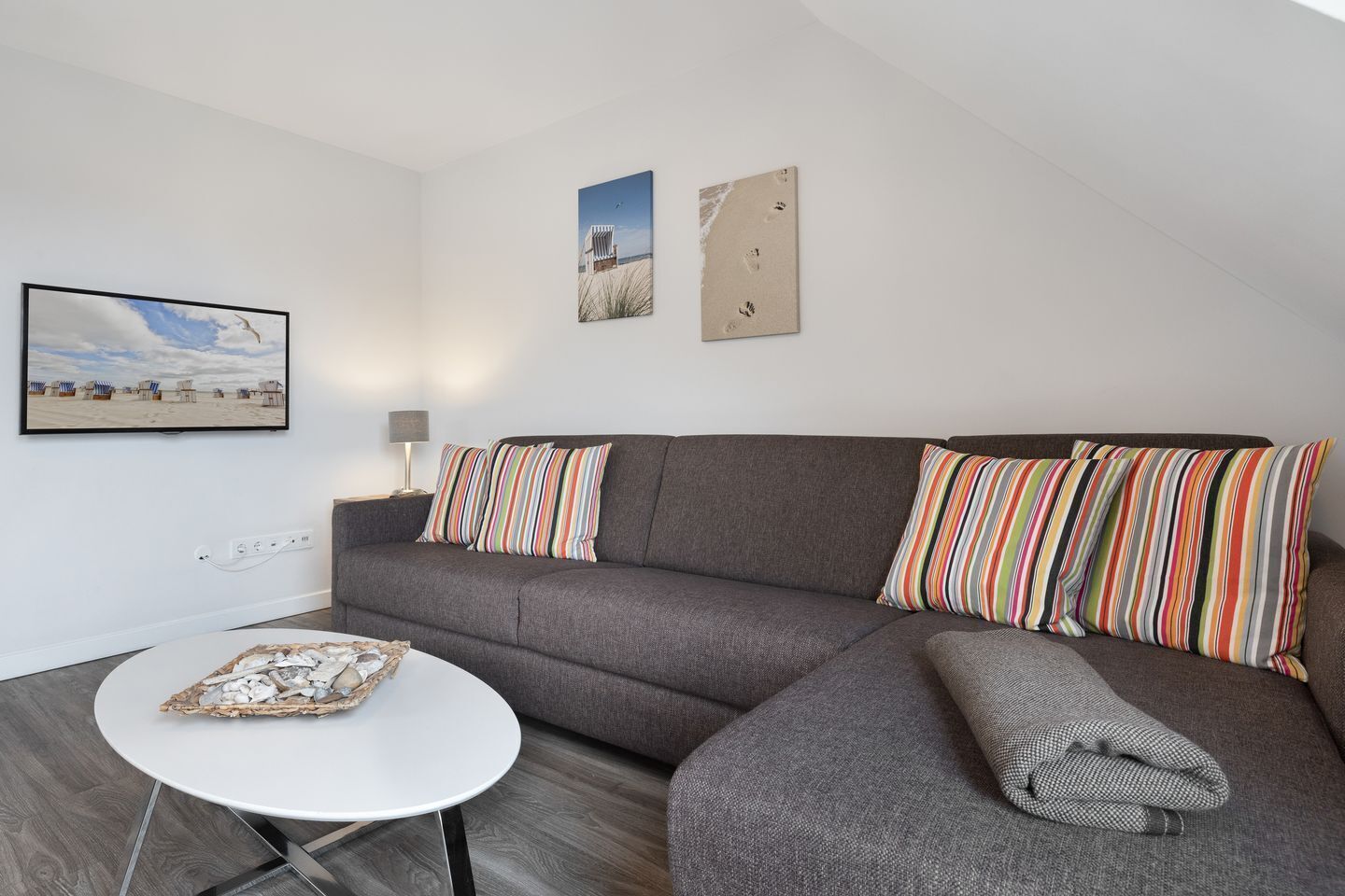 A modern living room with a grey sofa, striped pillows, a white coffee table, and artwork on the walls.
