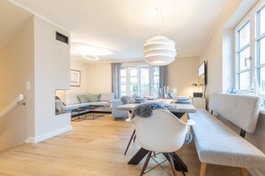 En moderne stue med spiseplads, der indeholder en sofa, et spisebord dækket til fire personer og et stort vindue, der giver naturligt lys.