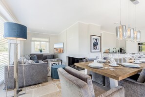 Et moderne spiseområde med et træbord dækket til seks personer, grå polstrede sofaer og en blå gulvlampe.