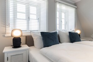 Et soveværelse med to senge, hvidt sengetøj og et natbord med en lampe.