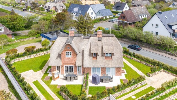 Ein zweistöckiges Haus mit einem Reetdach, einem Steinfundament und einem gepflegten Garten mit Rasen und Steinrändern.