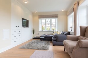 Ett modernt vardagsrum med en grå soffa, en beige fåtölj och ett soffbord. En platt-TV är monterad på väggen och det finns ett fönster med gardiner.