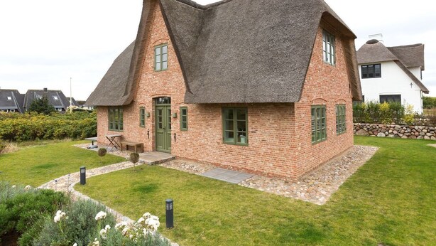 Une maison dotée d’un toit incurvé original, de murs en briques et d’un petit porche à l’avant.