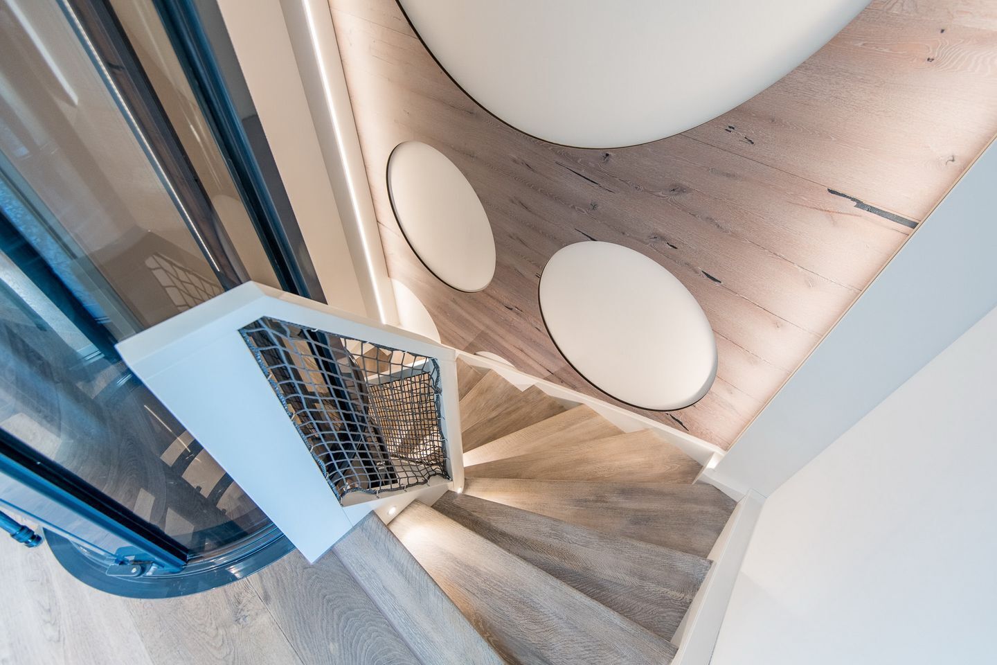 A modern staircase with a wooden finish and a glass door leading to a room.
