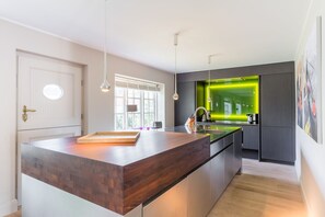 Et moderne køkken med en træø, hængende lamper og en bagvæg i grøn belysning.