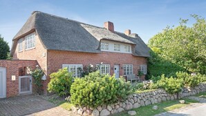 A traditional brick house with a thatched roof, a stone wall, and a well-maintained garden with shrubs and a bench. - Wattwai - Asia Kisses Keitum ! (Sylt / OT Keitum)