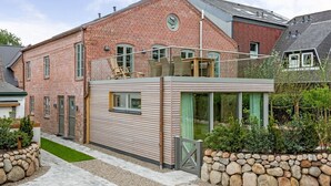 A modern brick house with a balcony, a small attached structure with large windows, and a stone wall garden. - Anno 1855 - Was für ein Highlight - Sowohl Außen als Auch Innen! (Sylt)