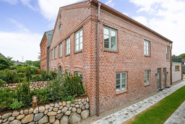 A red brick building with a stone wall garden, multiple windows, and a clear sky.