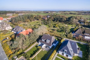An aerial view of a residential area with houses, a cemetery, and a lighthouse in the distance. - Lisas Hüs - Beste Lage Zwischen Dünen und Dorfteich. Tolles Grundstück und Viel Platz (Wenningstedt-Braderup (Sylt))