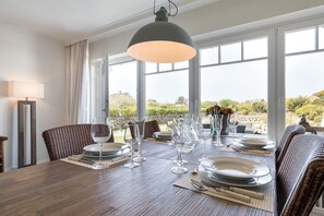 Een eethoek met een houten tafel voor zes personen, grote ramen en uitzicht op het omliggende landschap.
