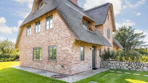 Une maison à deux étages, dotée d’un toit à forte pente, d’une façade en briques et de fondations en pierre.