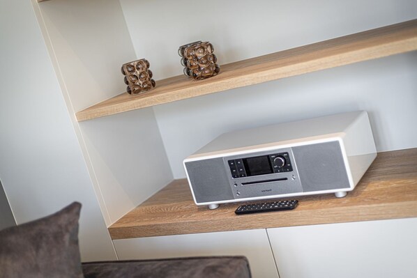 A modern living room with a wooden shelf holding a Sonora radio and a remote control.