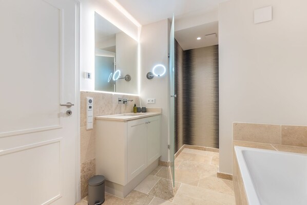 A modern bathroom with a glass shower enclosure, a standalone bathtub, and a vanity with a mirror.