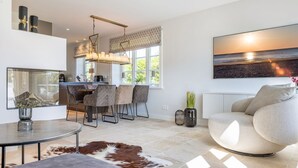 Un salon moderne avec une table basse ronde, un canapé et un coin repas comprenant des chaises, et une cuisine en arrière-plan.