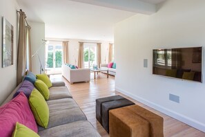 En moderne stue med sofa, skærmstole, sofabord og et fjernsyn ophængt på væggen.