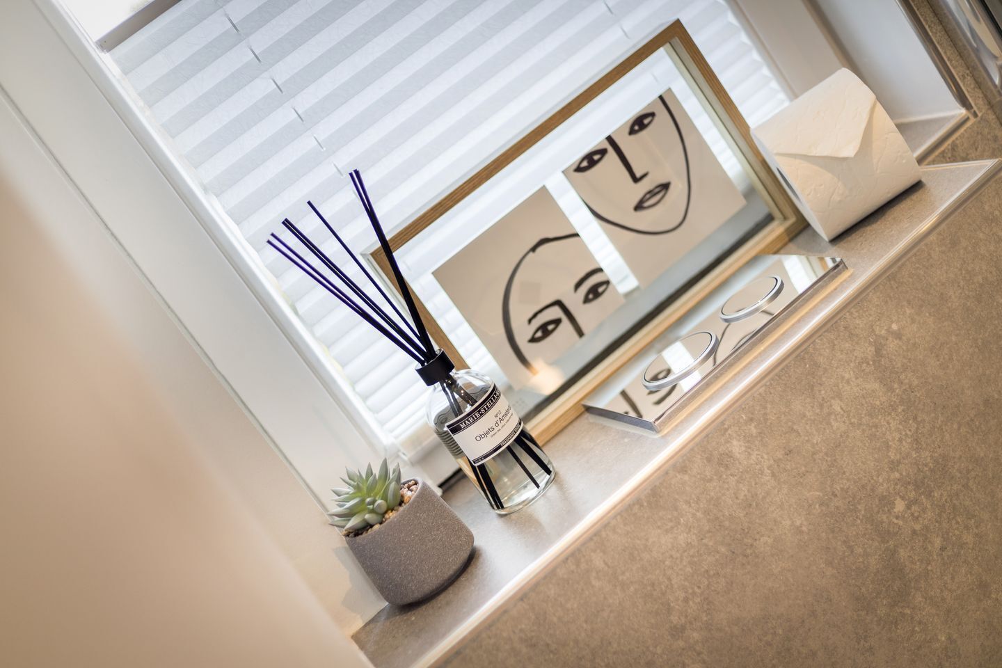 Un interior moderno con diseño minimalista, que incluye una planta pequeña en maceta, una botella decorativa y una obra de arte enmarcadas sobre una encimera.