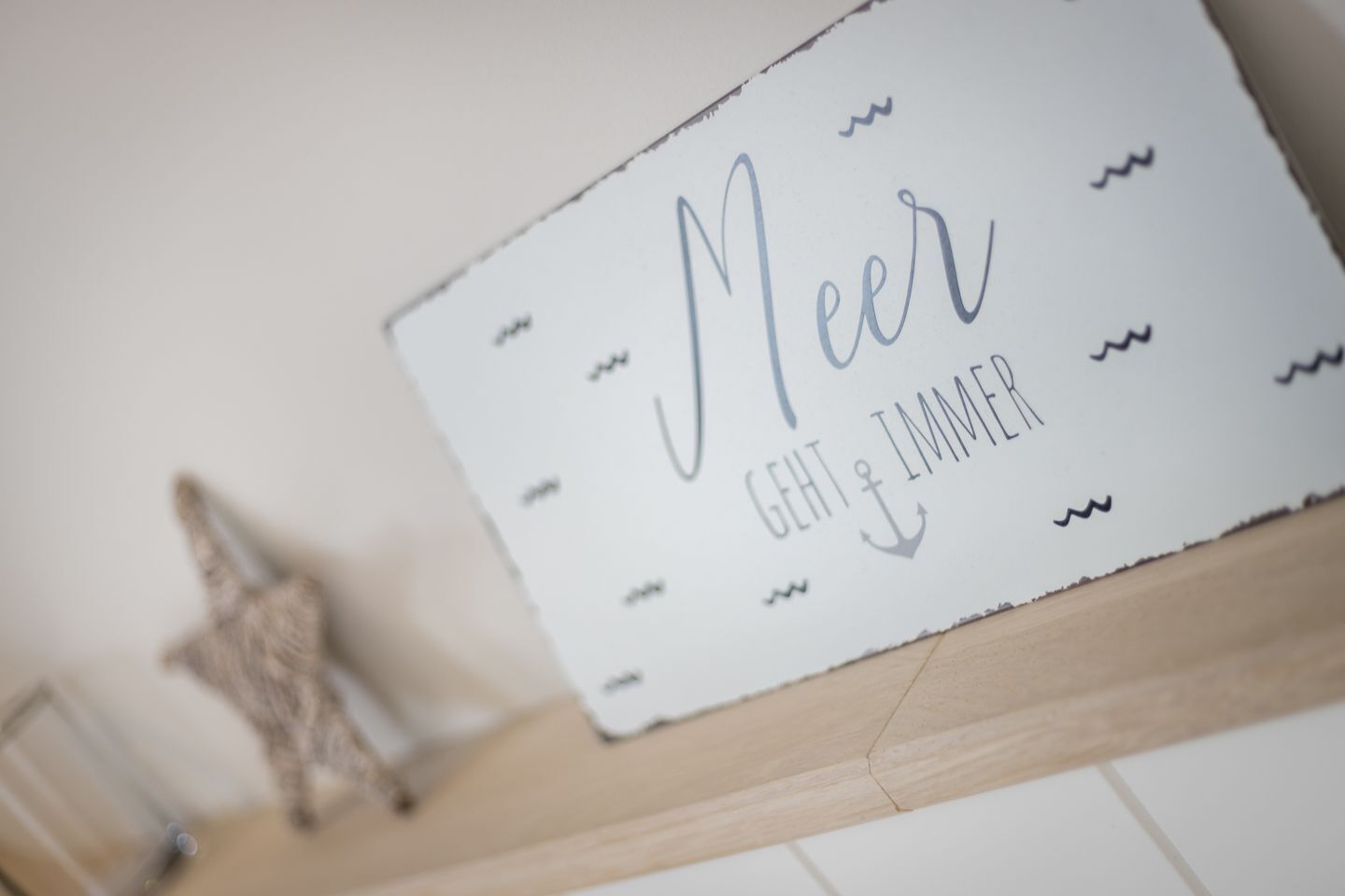 A sign with the words "Meer" and "GEHT IMMER" on a white background with a wooden shelf below.