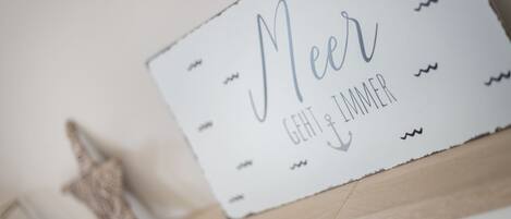 A sign with the words "Meer" and "GEHT IMMER" on a white background with a wooden shelf below.