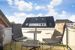 En tagterrasse med to liggestole, et lille bord og en metalstol.