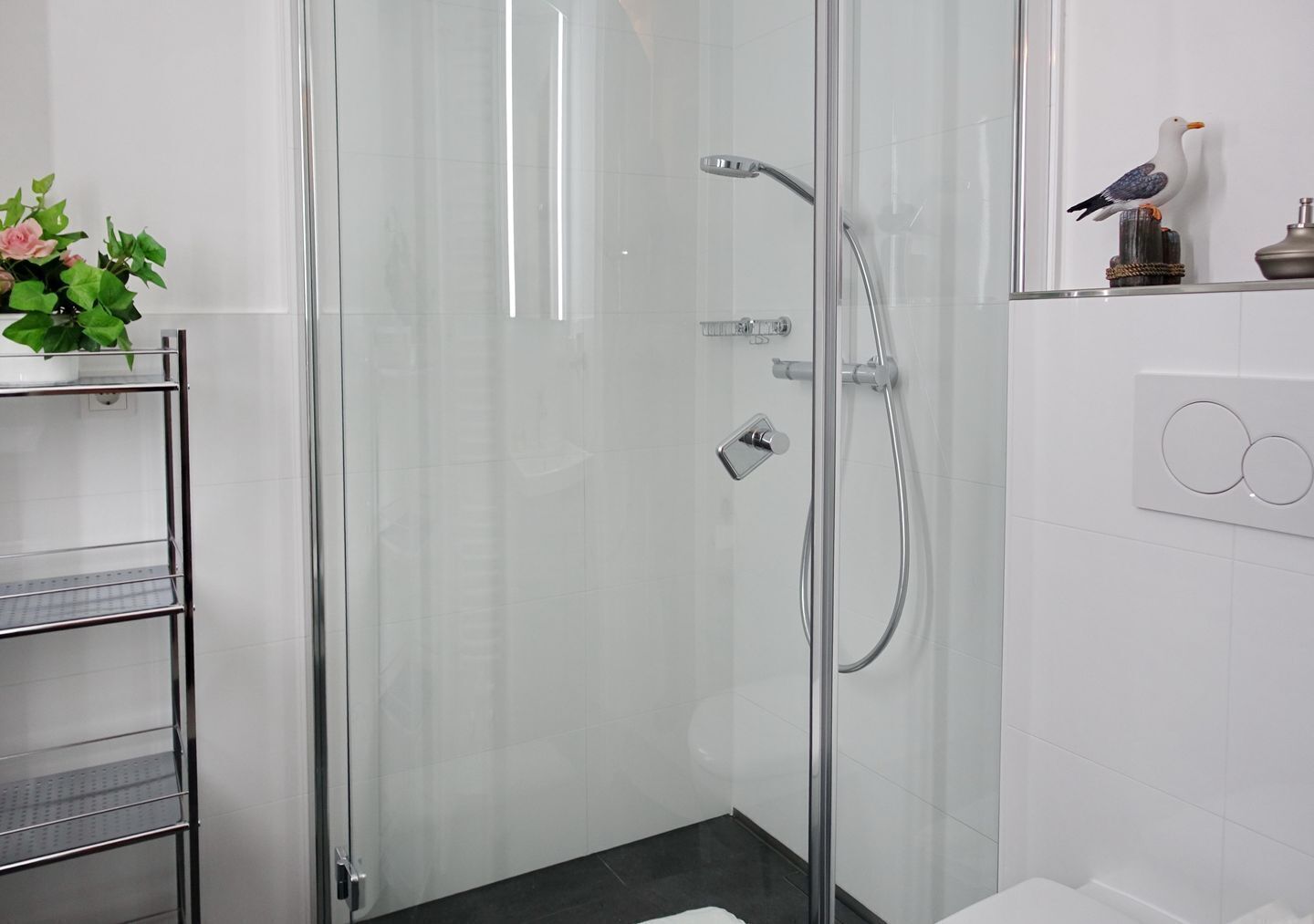 Une salle de bain moderne avec une douche à parois de verre, une étagère en métal et un luminaire fixé au mur.