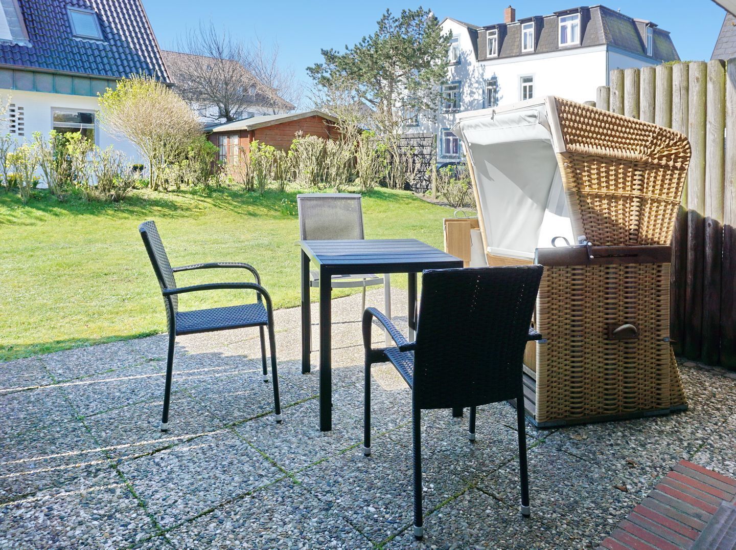 An outdoor patio with a table and two chairs, a wicker chair, and a white folding chair.