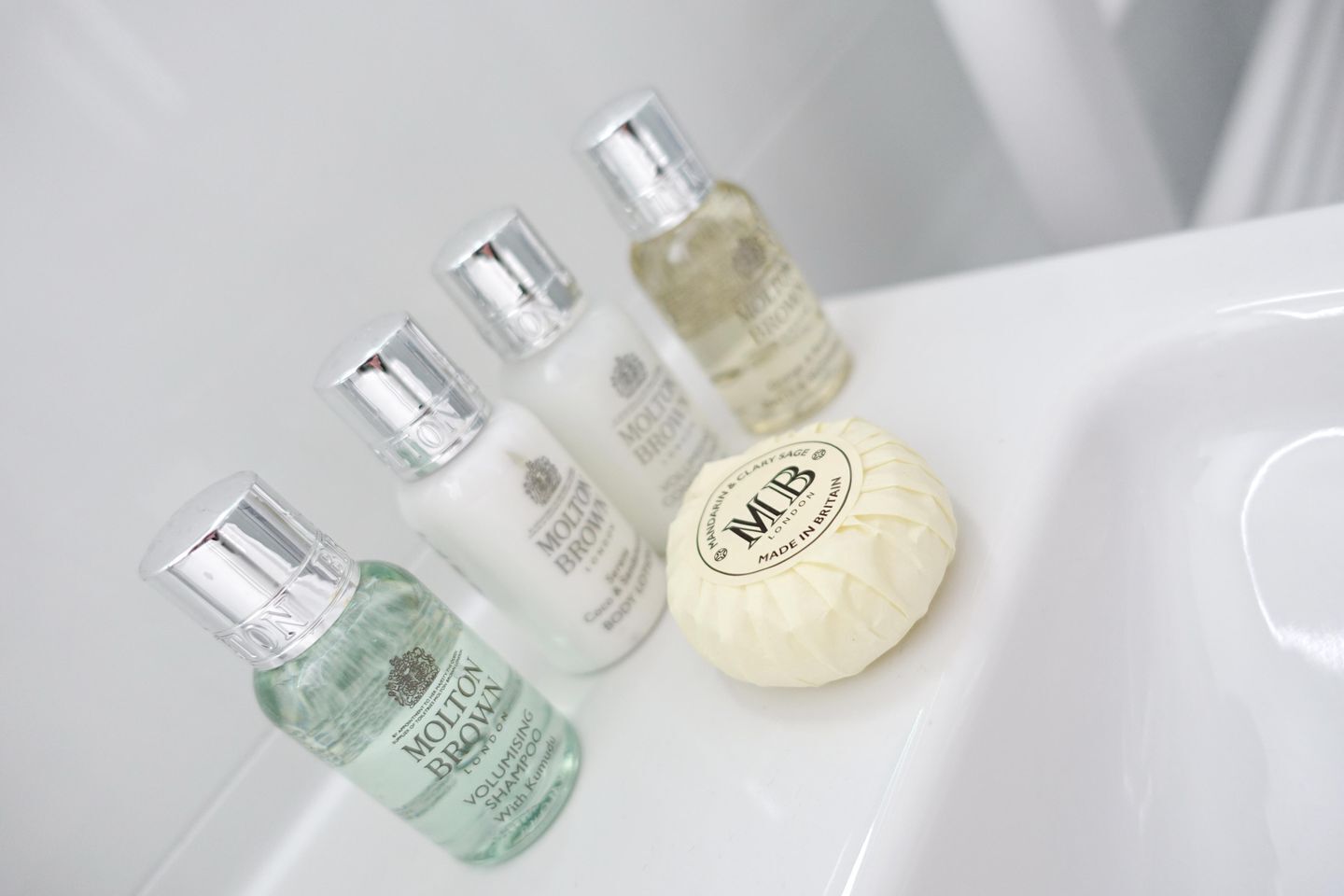 Four bottles of Molten Brown hair care products and a bar of soap on a white sink.