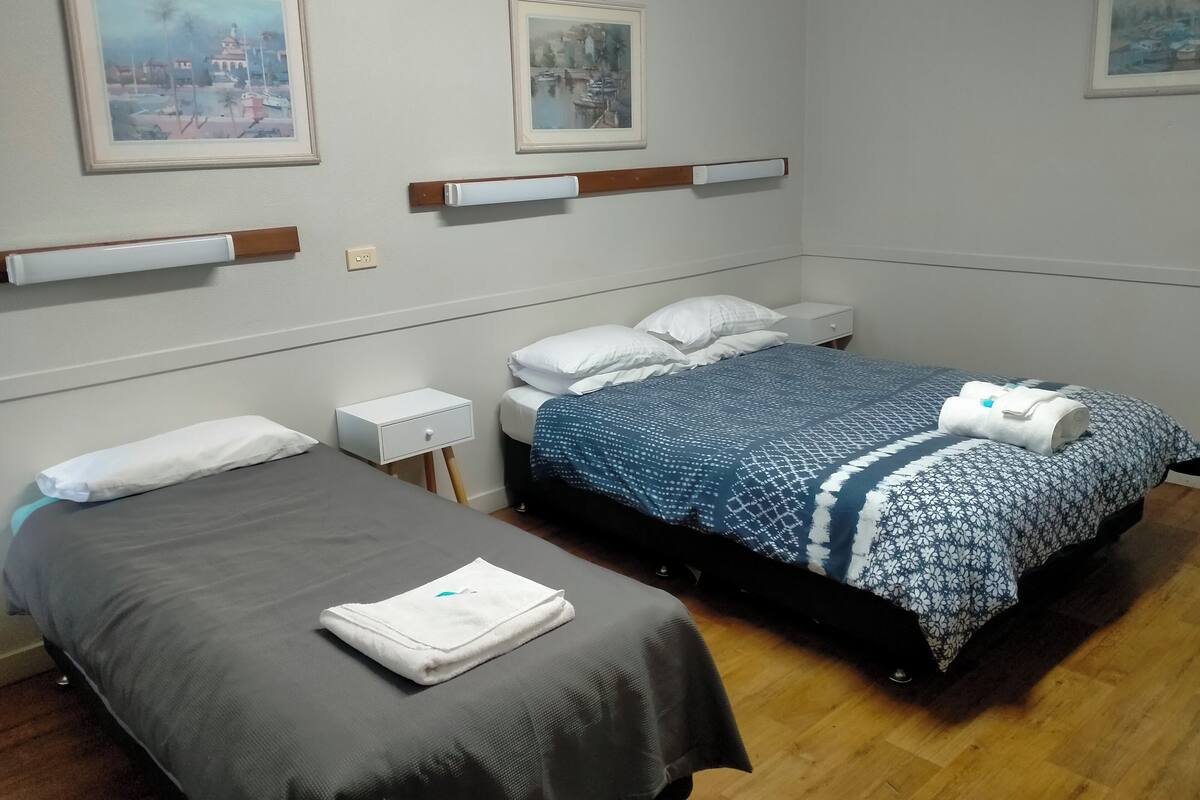 Une chambre d’hôtel avec deux lits simples, une petite table de chevet avec une lampe et une étagère fixée au mur.