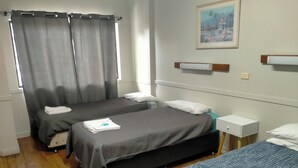 Une chambre d’hôtel avec deux lits simples, une petite table de chevet avec une lampe, une fenêtre avec des rideaux et un tableau au mur.