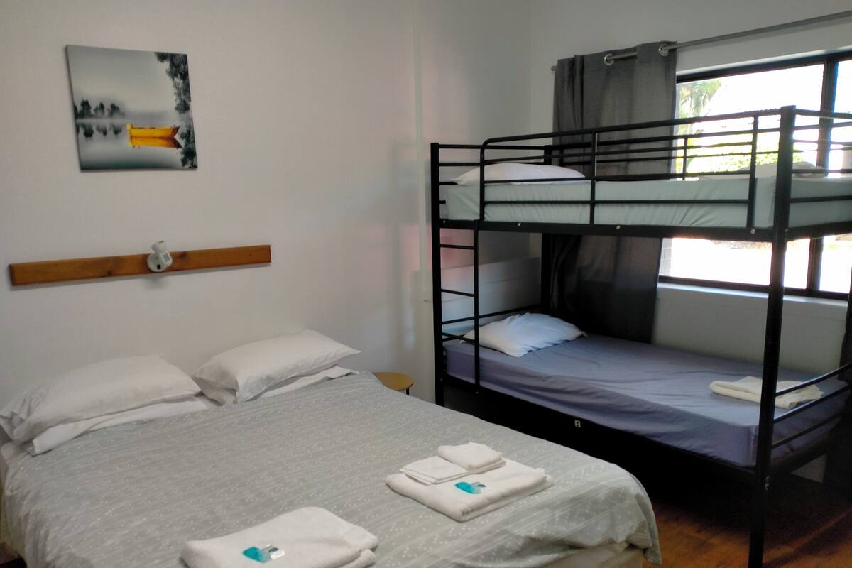 Une chambre avec un lit superposé et un lit simple. Il y a un tableau au mur et une fenêtre avec des rideaux.
