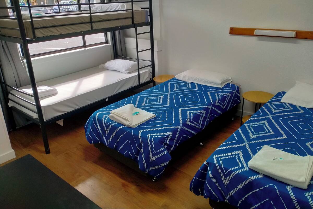 Une chambre de dortoir avec des lits superposés, deux lits simples, une petite table et une fenêtre donnant sur la rue.