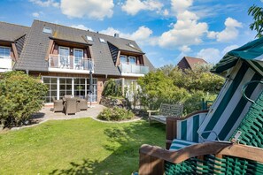 Una casa de dos pisos con un balcón, un patio con mobiliario exterior y un jardín bien cuidado.