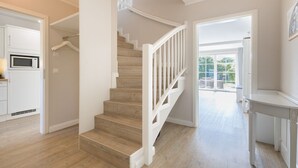 Una cocina moderna con armarios blancos, un microondas y una escalera de madera con barandillas blancas que lleva a un balcón.