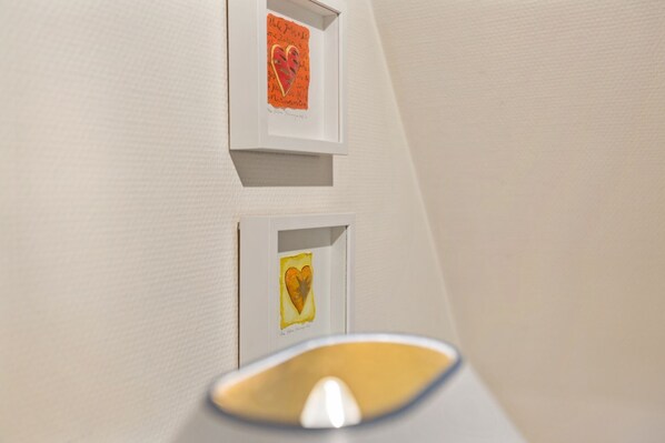 A wall with two framed artworks, one above the other, and a light fixture in the foreground.