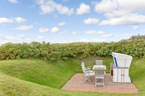 A patio with a table and chairs, surrounded by a hedge and a brick pathway. - Seeblick - Sylt Royal. Sie Wohnen Direkt am Meer (Wenningstedt-Braderup (Sylt))