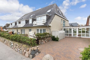 A two-story house with a brick exterior, a stone retaining wall, and a paved driveway. - Beachhouse Lornsen-hof, App 7 - Lage, Lage, Lage! Das Beachhouse Lornsenhof Müssen Sie Einfach (Sylt)