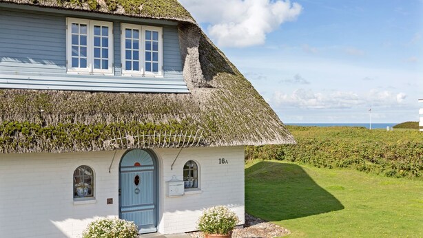 Un bâtiment blanc avec un toit de chaume, une porte bleue et le numéro 16A.