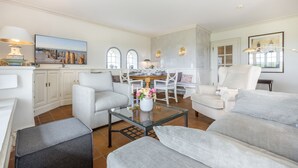 Un salon spacieux comprenant un coin repas, des meubles blancs et une grande fenêtre offrant une vue dégagée.