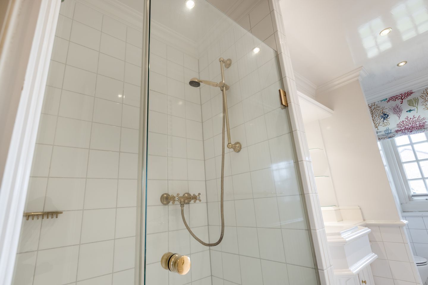 Een douchecabine met glazen wanden, een handdouche en een bediening op de muur.