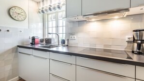 Une cuisine moderne avec des armoires blanches, un comptoir noir, une machine à café en acier inoxydable et une horloge au mur.