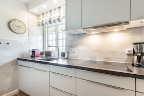 Ett modernt kök med vita skåp, en svart bänkskiva, en kaffebryggare i rostfritt stål och en klocka på väggen.