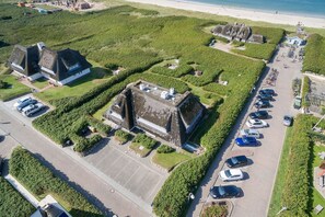 An aerial view of a coastal property with a parking lot, a beach, and several buildings with thatched roofs. - Villa Bellevue - Schönste Aussichten! (Wenningstedt-Braderup (Sylt))