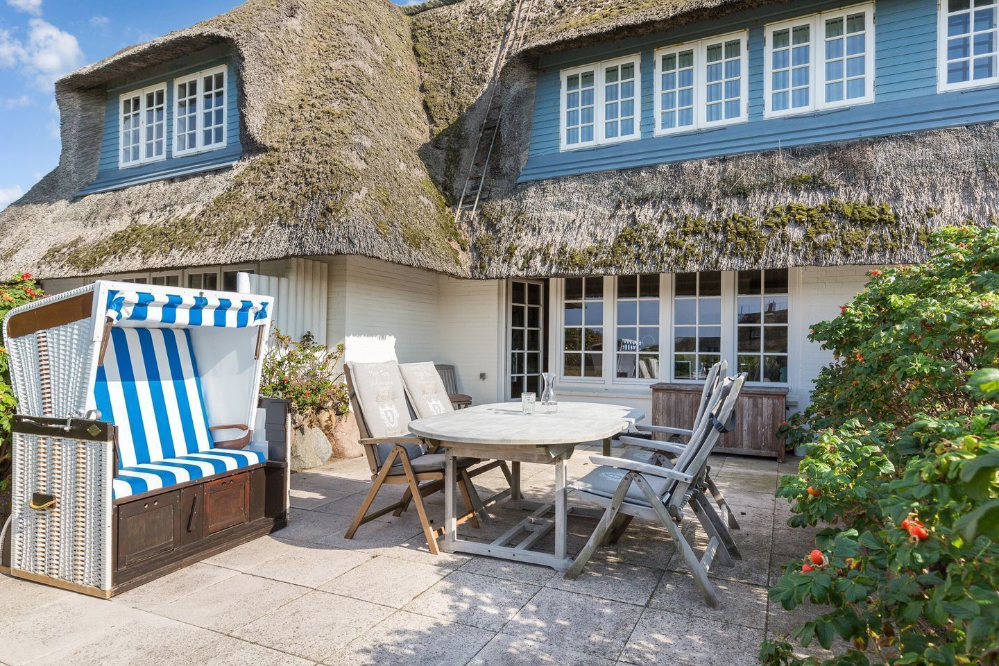 A thatched-roof house with a dining area, a striped chair, and a table.