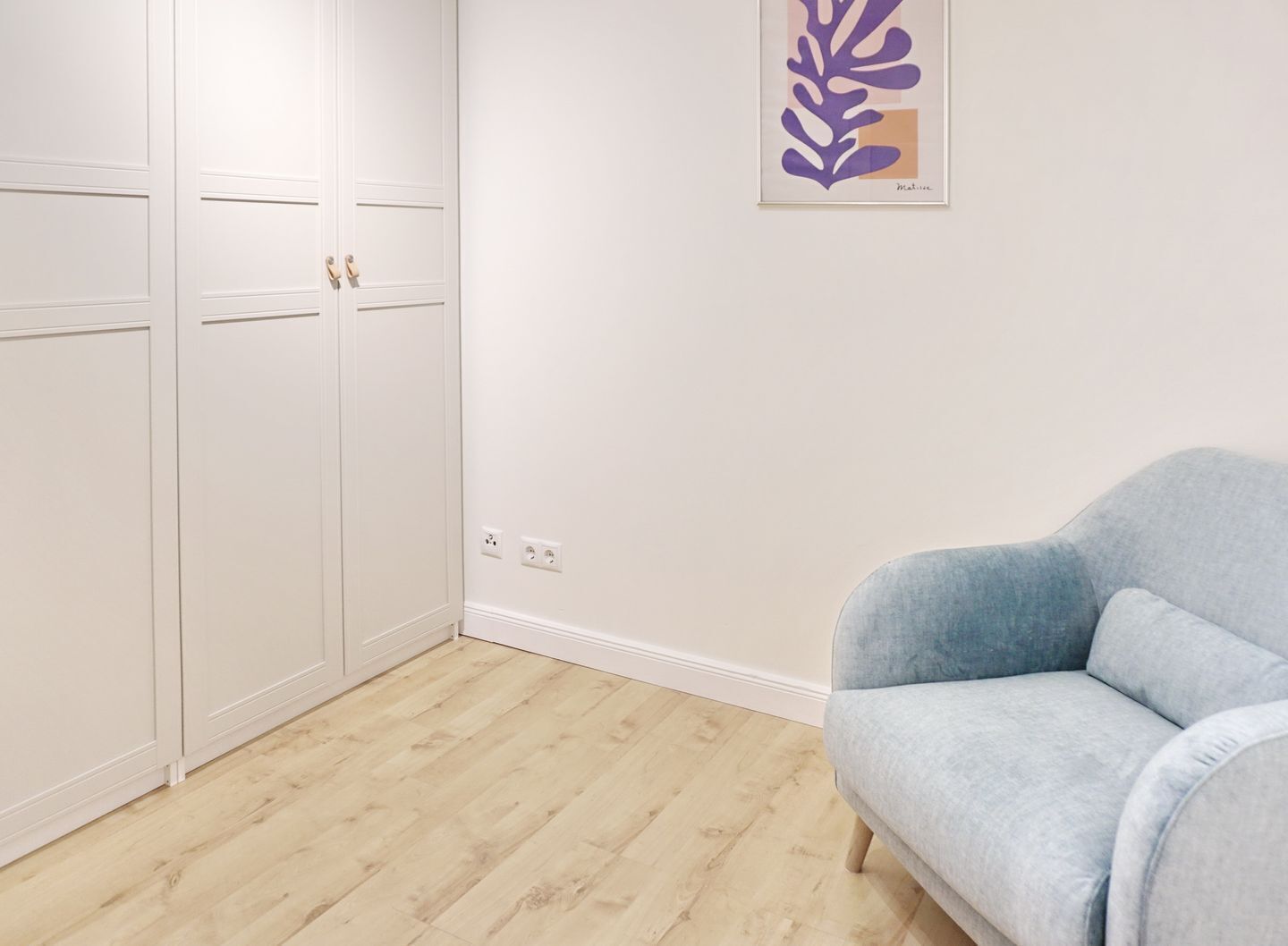 Ein Zimmer mit einem hellblauen Sofa, einem weißen Kleiderschrank und einem an der Wand befestigten Kunstwerk.